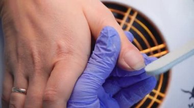 Close-up of manicure master in blue gloves filing nails with special nail file.