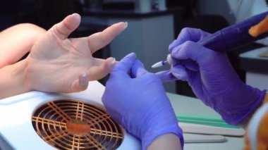 A manicure master in blue gloves removes gel polish from nails using a cutter.