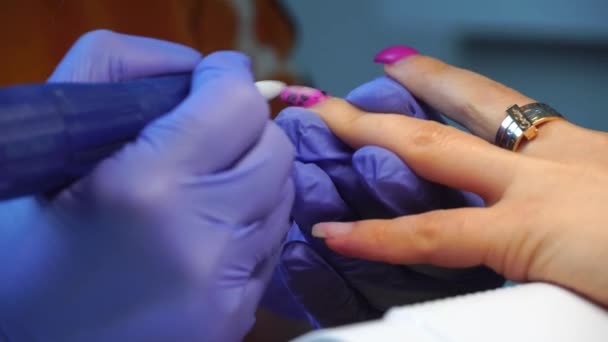 Manicure master in blue gloves removes gel polish from nails using a cutter. — Stockvideo