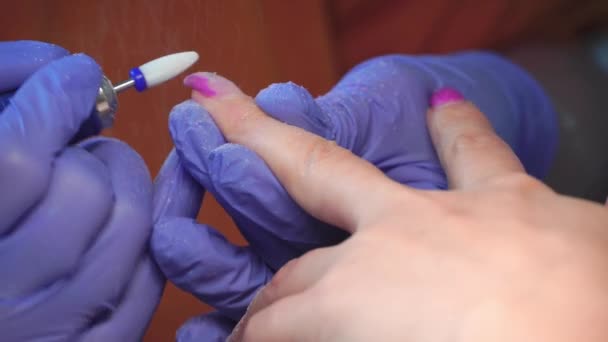Le maître manucure en gants bleus enlève le gel poli des ongles à l'aide d'un cutter. — Video