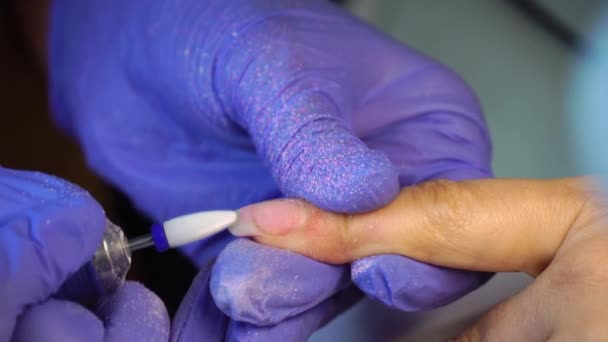 Manicure master in blue gloves removes gel polish from nails using a cutter. — Video Stock