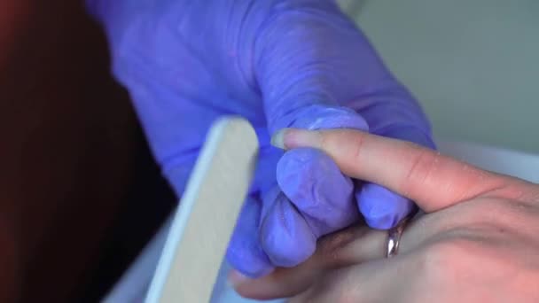 Close-up of manicure master in blue gloves filing nails with special nail file. — Vídeo de Stock
