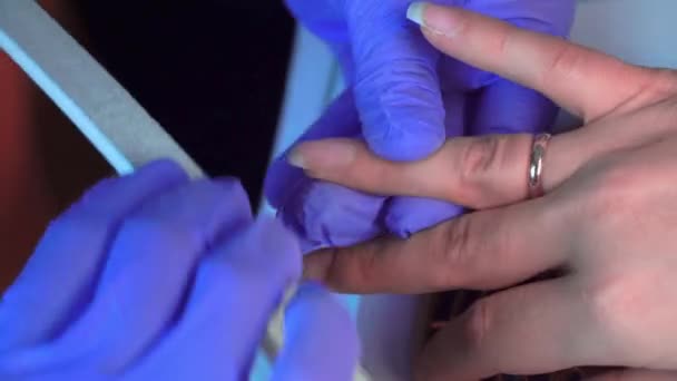 Close-up of manicure master in blue gloves filing nails with special nail file. — Stockvideo