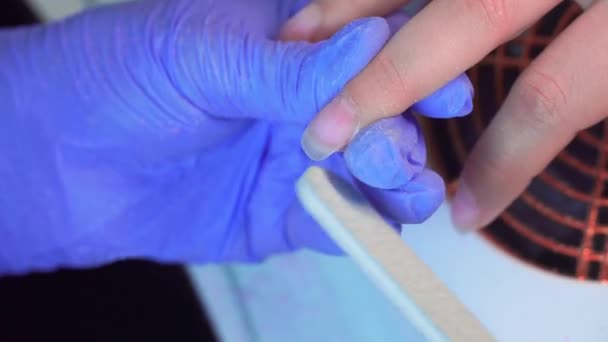 Close-up of manicure master in blue gloves filing nails with special nail file. — Wideo stockowe