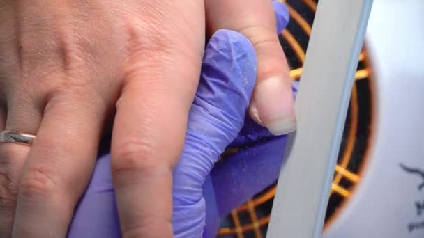 Close-up of manicure master in blue gloves filing nails with special nail file. — Stock video