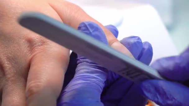 Gros plan du maître manucure en gants bleus lime à ongles avec lime à ongles spéciale. — Video