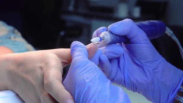 A manicure master in blue gloves removes gel polish from nails using a cutter. — Videoclip de stoc