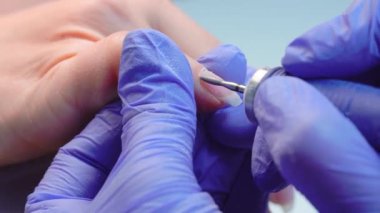 hands of manicure master in blue gloves use an electric nail file remove cuticle