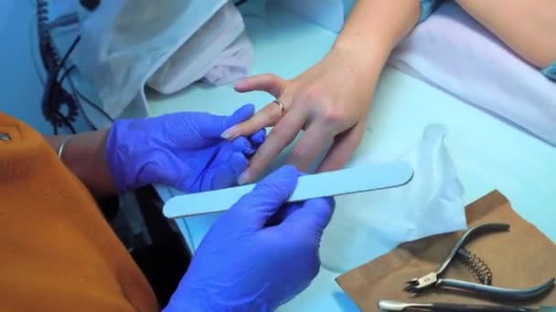 Close-up of manicure master in blue gloves filing nails with special nail file — Video Stock