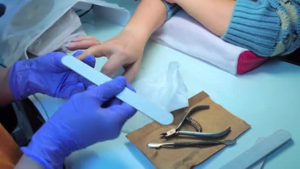 Close-up of manicure master in blue gloves filing nails with special nail file — Stock videók