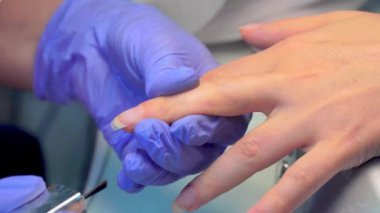 close-up of manicure master applies layer of pink gel polish to client's nail.