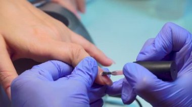 close-up of manicure master applies layer of pink gel polish to client's nail.