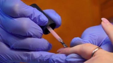 close-up of manicure master applies layer of pink gel polish to client's nail.