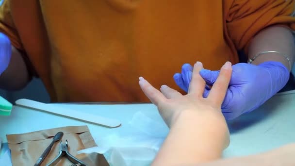 Close-up of manicure master in blue gloves filing nails with special nail file — Vídeo de stock