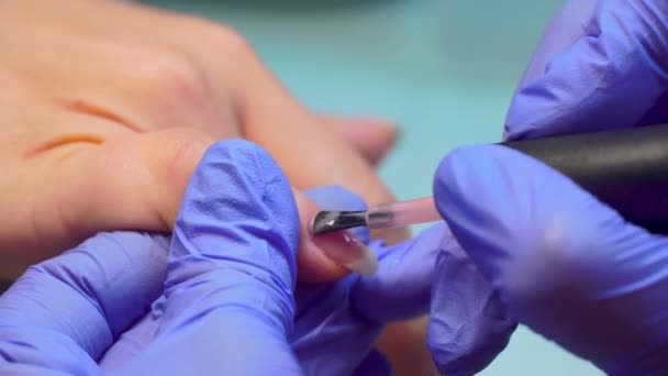 Close-up of manicure master applies layer of pink gel polish to client's nail. — Stock video