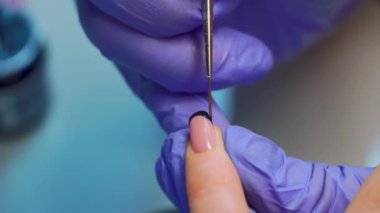 close-up of a manicurist paints a black French on the client's nails with a brush.