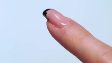 close-up of a manicurist paints a black French on the client's nails with a brush.