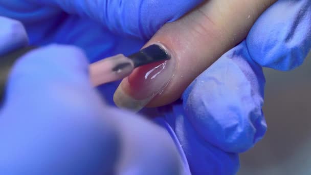 Close-up του master μανικιούρ εφαρμόζει στρώμα ροζ βερνίκι τζελ στα νύχια του πελάτη. — Αρχείο Βίντεο