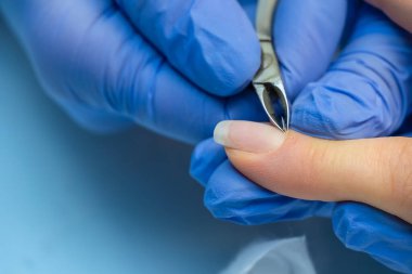 Mavi eldivenli bir manikür ustasının yakın çekimi bir kadın için manikür yapar, profesyonel tırnak maşasıyla tırnak derisini keser. Bir güzellik salonunun kliniğinde profesyonel manikür..