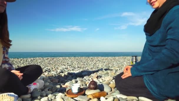 Two women are preparing for tea ceremony. sitting in lotus position on seashore. — Αρχείο Βίντεο