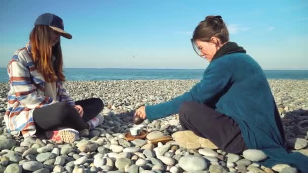 Two women are preparing for tea ceremony. sitting in lotus position on seashore. — Vídeo de stock