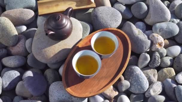 Close-up of two poured cups of tea on a wooden tray, brown teapot, — стоковое видео