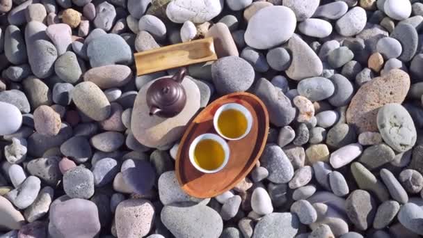 Close-up of two poured cups of tea on a wooden tray, brown teapot, — Video