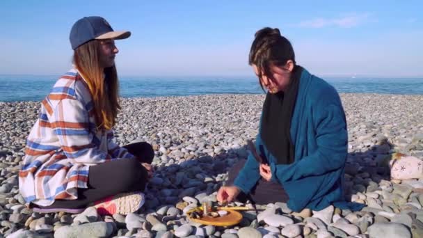 Two women are sitting on the seashore and preparing for a rape ceremony. — Stockvideo