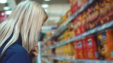Bir kadın süpermarkette bir paket cips seçer. Mağazadan alışveriş..