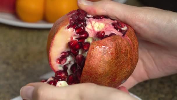 Weibliche Hände schälen einen Granatapfel über einem Teller auf dem Tisch, Nahaufnahme. — Stockvideo