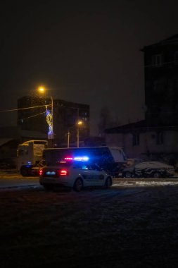 Karlı bir şehir caddesinde, gece trafikte bir polis arabası. Dikey fotoğraf