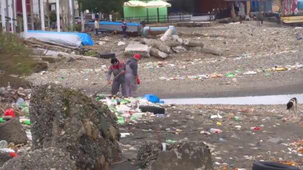 Plastikmüll wurde von der Flut an Land gespült. Zwei Arbeiter packen Müll in Säcke — Stockvideo