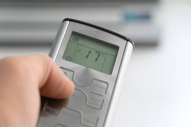 Klimayı gösteren gri bir uzaktan kumandayla bir adamın eline yakın çekim.