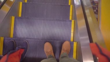 Bir adam ve bir kadın yürüyen merdivenden iniyorlar. Bacakların üst görünümü.