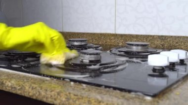 Sarı eldivenli ev hanımı mutfakta gaz sobasını süngerle yıkıyor..