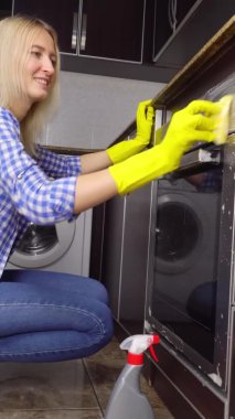Sarı lastik eldivenli kadın gaz sobasını sarı süngerle temizliyor..