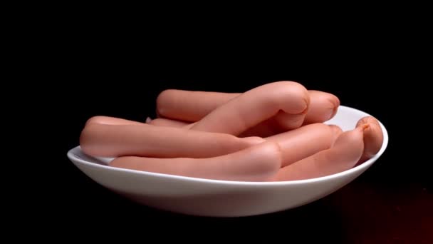 Sausages spinning on a white plate on a black background. Stock