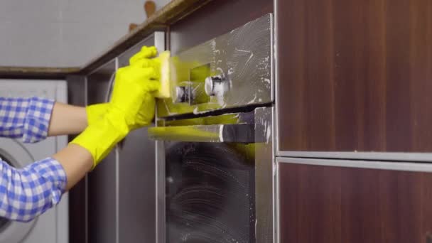 Hemmafru kvinna i gula handskar tvättar gasspis i kök med svamp. — Stockvideo