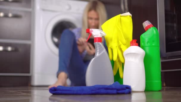 Frau, die auf dem Boden sitzt und ihr Handy aus dem Fokus nimmt. Flaschen Reinigungsmittel — Stockvideo