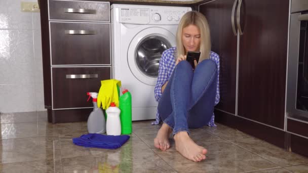 Kotlu ve gömlekli sarışın mutfak zemininde çamaşır makinesinin yanında oturuyor. — Stok video