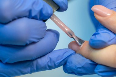 Mavi eldivenli bir manikür ustasının yakın çekimi müşterinin tırnağına pembe jel cilası sürüyordu. Tırnak cilasıyla oje sürüyorum. Güzellik salonunda profesyonel manikür..