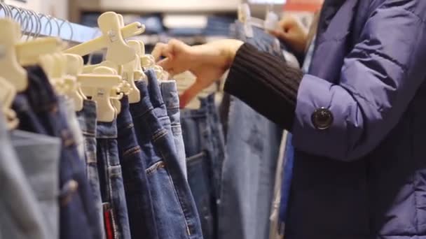 Hands of young woman choose jeans that hang on hanger in clothing store. — Stock Video
