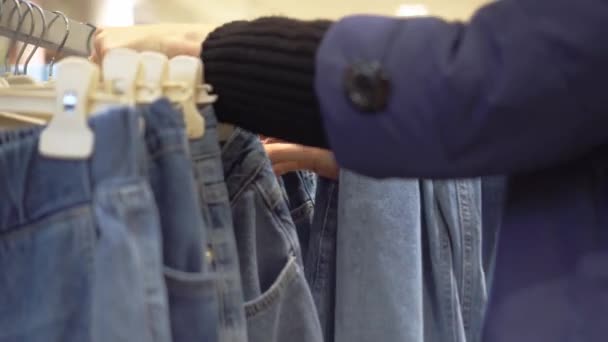 Handen van jonge vrouw kiezen jeans die hangen op hanger in kledingwinkel. — Stockvideo