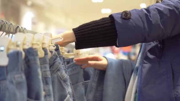 Handen van jonge vrouw kiezen jeans die hangen op hanger in kledingwinkel. — Stockvideo