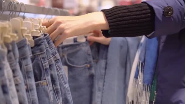 Handen van jonge vrouw kiezen jeans die hangen op hanger in kledingwinkel. — Stockvideo