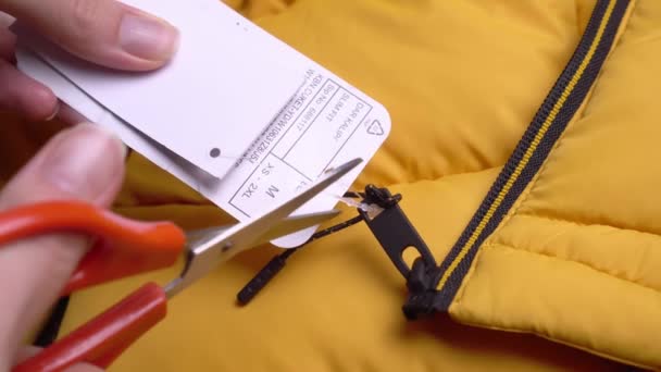 Руки девушки снимают ценник с желтой куртки ножницами. — стоковое видео