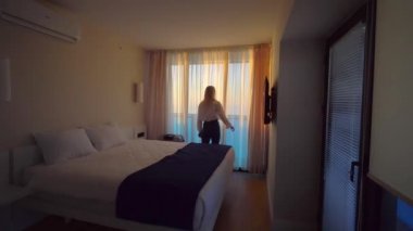 Genç bir kadın bavuluyla odaya girer, dantel bir perde açar.,