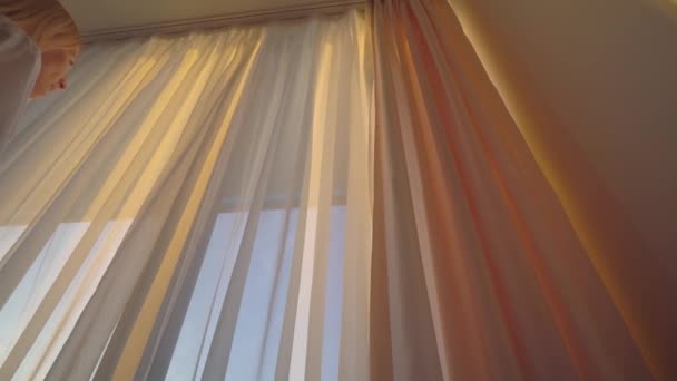 Nő kinyitja függönyök és néz napfelkelte, naplemente napsugarak esik sziluett — Stock videók