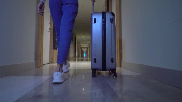 Woman walks down corridor of hotel and rolls suitcase with luggage on wheels. — Stock Video