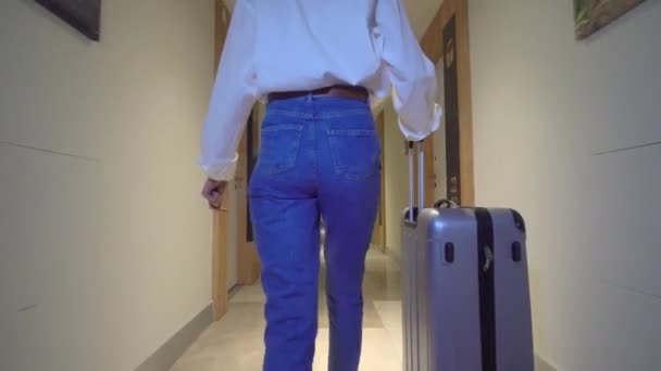 Rear view of woman walking down corridor of hotel. rolls her luggage behind her — Stock Video